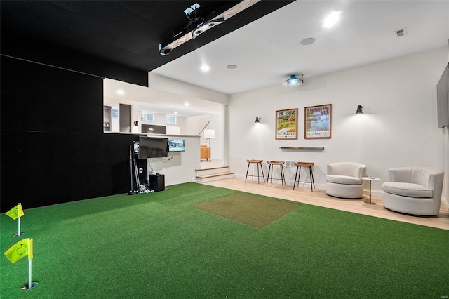interior space with golf simulator, visible vents, and wood finished floors