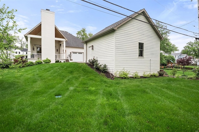 rear view of house featuring covered porch, a yard, a chimney, and a garage