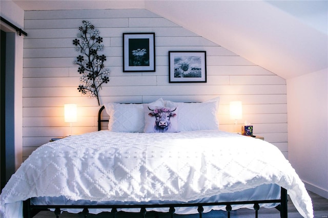 bedroom featuring baseboards, wood walls, a barn door, and vaulted ceiling