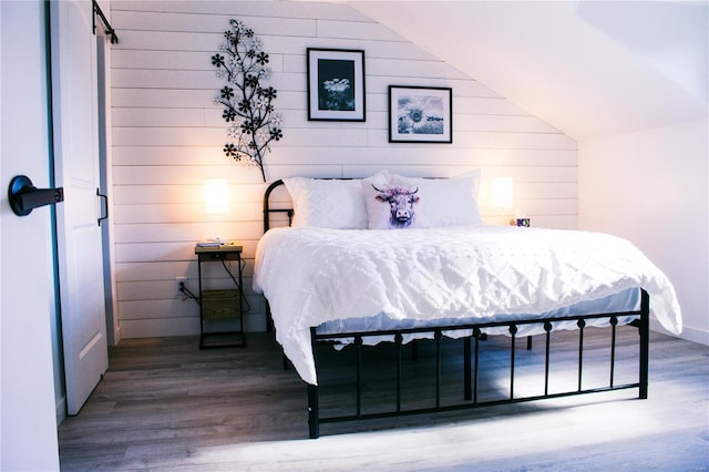 bedroom with lofted ceiling, wooden walls, and wood finished floors