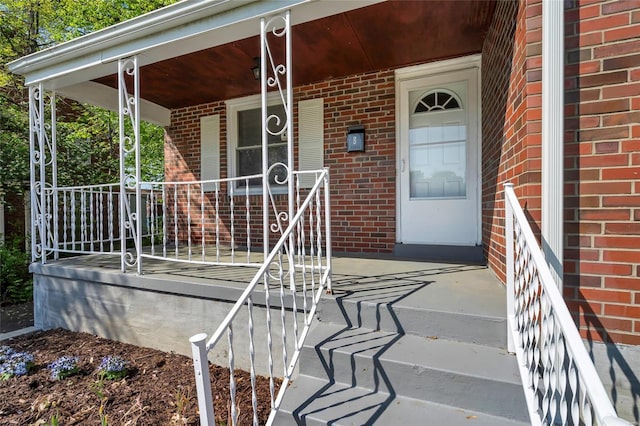 doorway to property with a porch and brick siding