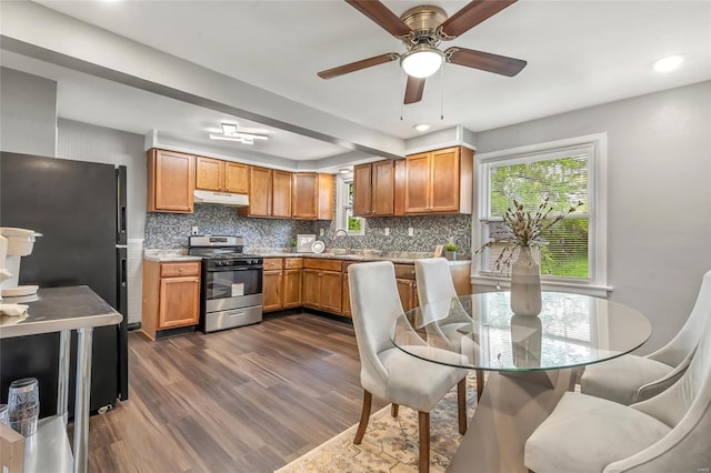 kitchen with freestanding refrigerator, gas range, dark wood-type flooring, backsplash, and under cabinet range hood