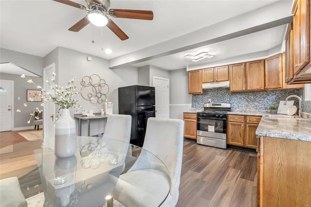 kitchen with freestanding refrigerator, under cabinet range hood, gas stove, a sink, and dark wood-style floors