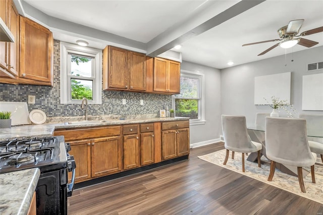 kitchen featuring brown cabinetry, visible vents, a sink, backsplash, and black gas range