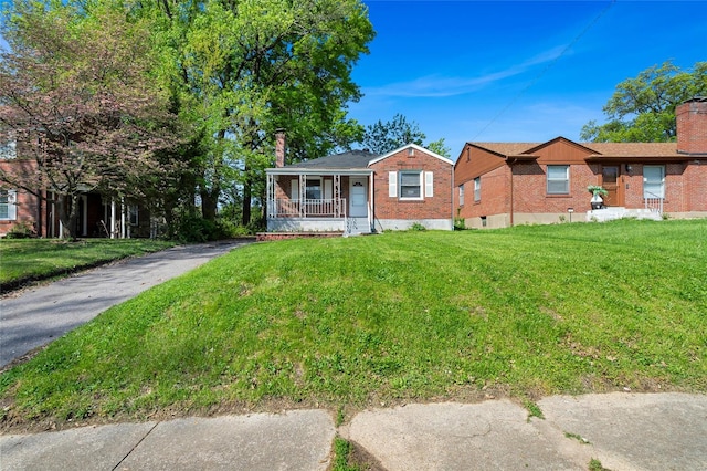 view of front of house with covered porch, aphalt driveway, brick siding, a front yard, and a chimney
