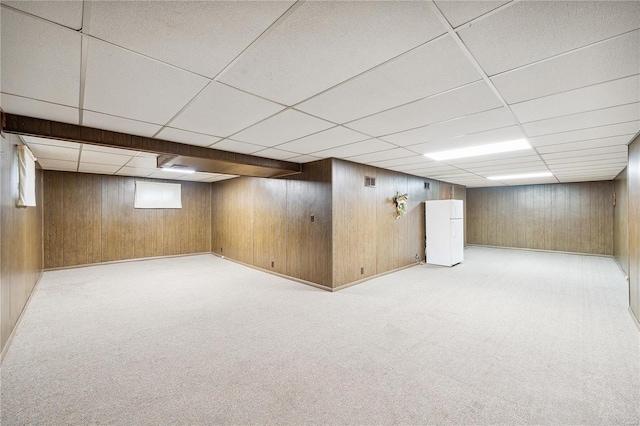 basement featuring light carpet, wood walls, and a paneled ceiling