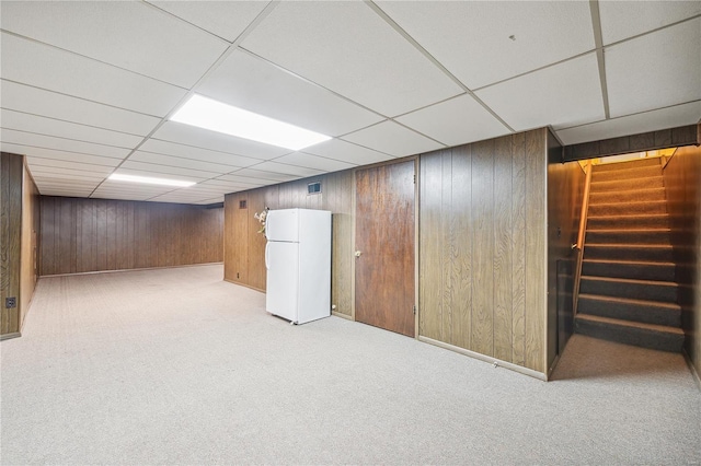 finished basement featuring freestanding refrigerator, carpet, wood walls, and stairs
