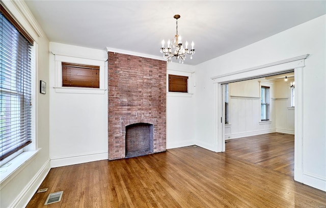 unfurnished living room featuring a notable chandelier, a fireplace, visible vents, and wood finished floors