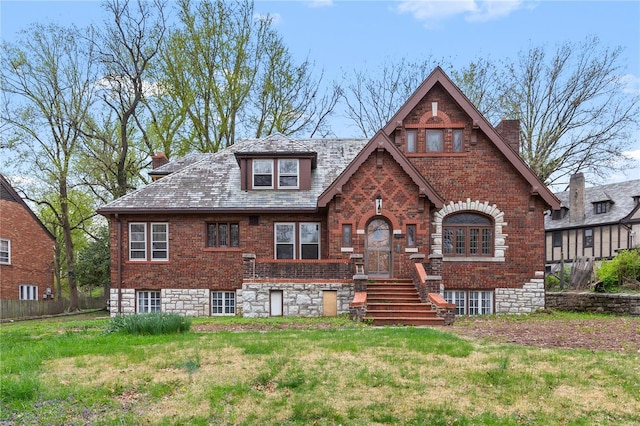 english style home with a high end roof, brick siding, a chimney, and a front yard