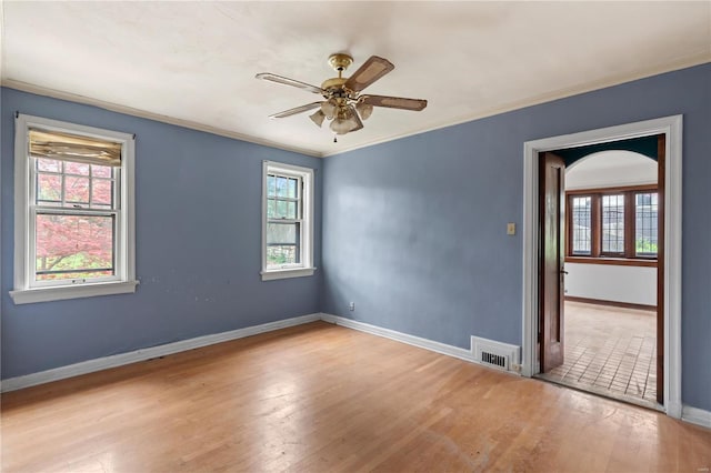 spare room featuring wood finished floors, a ceiling fan, crown molding, visible vents, and baseboards