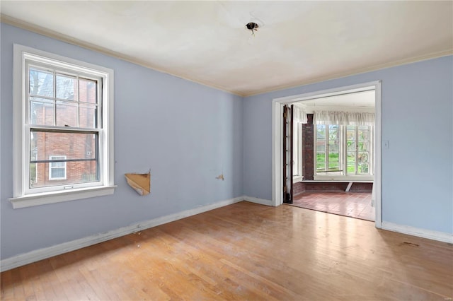 empty room with crown molding, wood finished floors, and baseboards