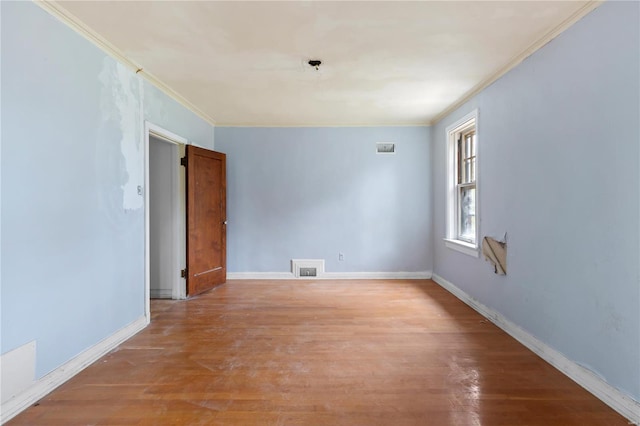 empty room with crown molding, light wood-type flooring, visible vents, and baseboards