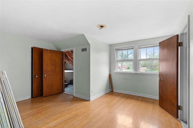 unfurnished bedroom featuring lofted ceiling, a closet, light wood-type flooring, visible vents, and baseboards