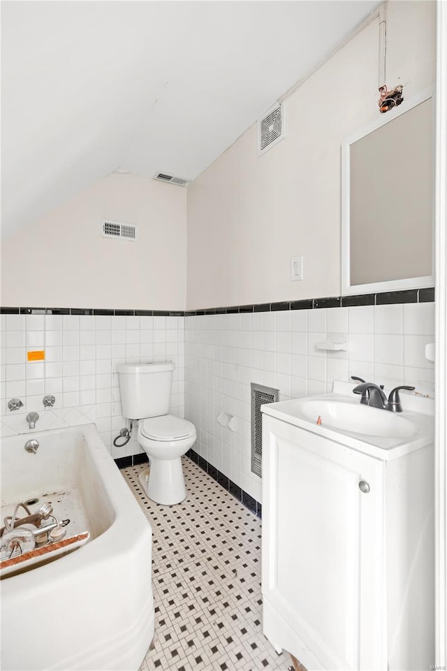 full bathroom with toilet, tile walls, visible vents, vaulted ceiling, and a garden tub