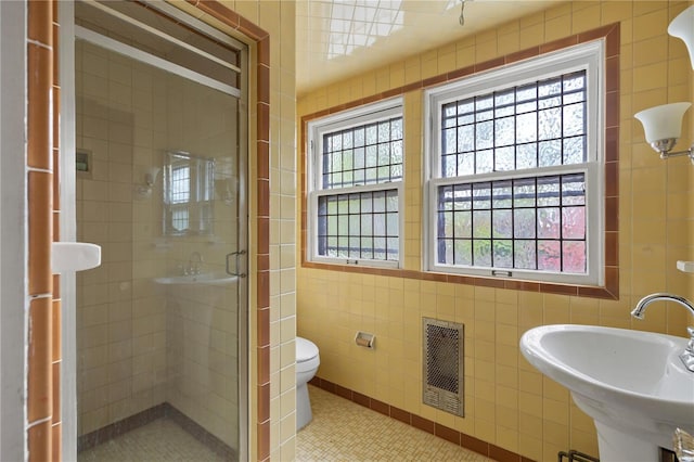 bathroom with tile walls, visible vents, a sink, a shower stall, and tile patterned flooring