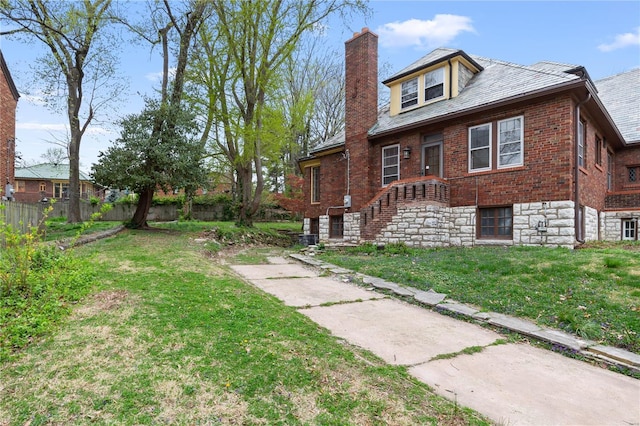 view of property exterior with fence, a high end roof, brick siding, a chimney, and a lawn