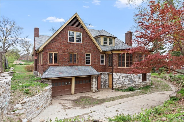 back of house featuring stone siding, driveway, a chimney, and a garage