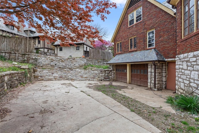 view of property exterior featuring fence, a garage, and stone siding