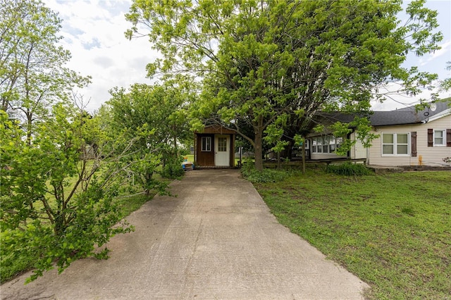 obstructed view of property featuring driveway, an outdoor structure, a front lawn, and a storage shed