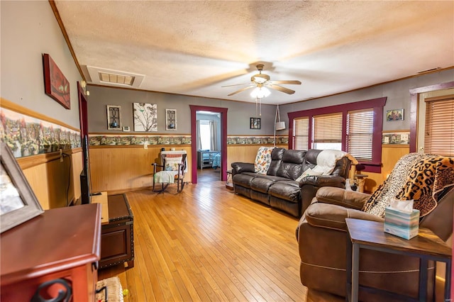 living area with a wainscoted wall, a textured ceiling, a ceiling fan, and visible vents
