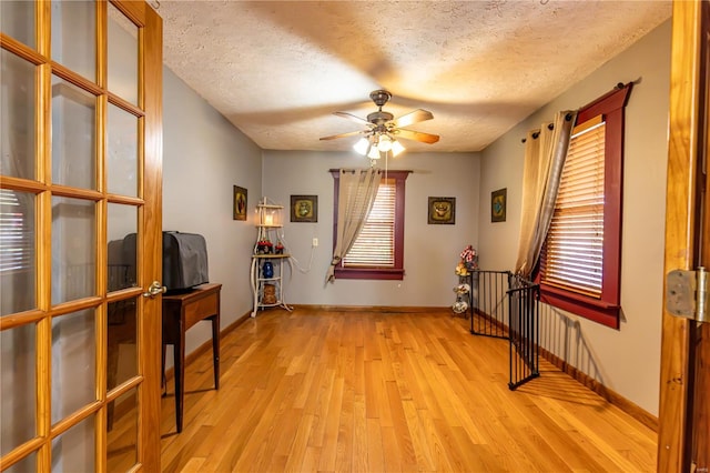 interior space featuring baseboards, light wood-style flooring, ceiling fan, and a textured ceiling