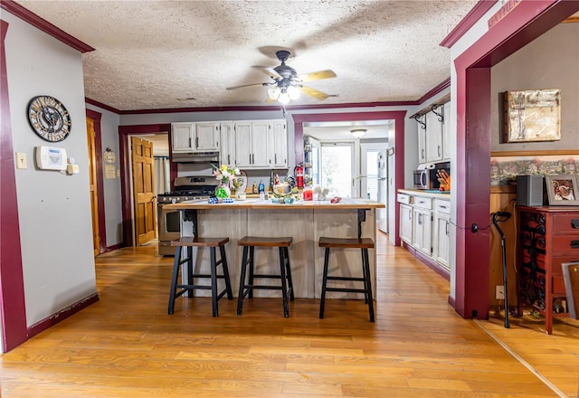 kitchen featuring stainless steel range with gas stovetop, a breakfast bar, ornamental molding, and white cabinets