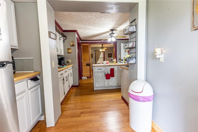 kitchen featuring light wood finished floors, freestanding refrigerator, white cabinets, a textured ceiling, and ceiling fan