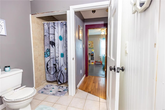 full bath with toilet, tile patterned flooring, ceiling fan, baseboards, and tiled shower