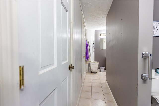 corridor featuring baseboards, light tile patterned flooring, and a textured ceiling
