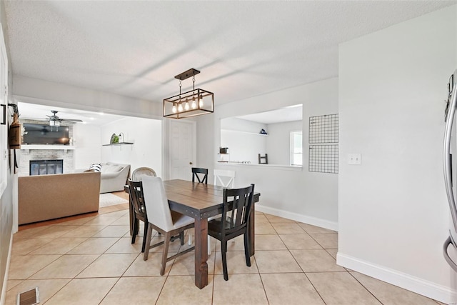 dining space featuring light tile patterned floors, a stone fireplace, baseboards, ceiling fan, and visible vents