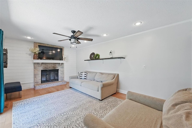living room with a ceiling fan, a fireplace, a textured ceiling, and wood finished floors