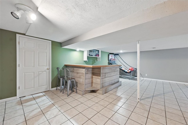 bar featuring a dry bar, baseboards, light tile patterned floors, and a textured ceiling