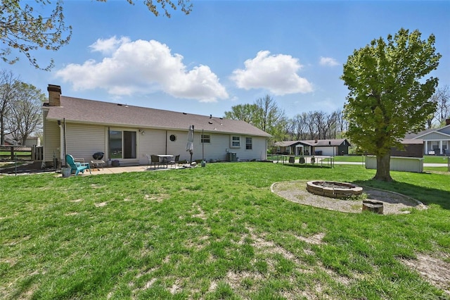 back of house with a chimney, a patio area, a fire pit, and a yard