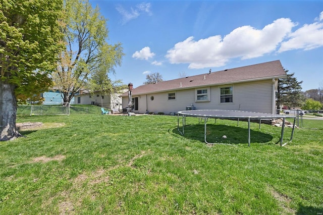 back of property with fence, a trampoline, and a lawn