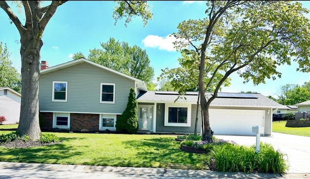split level home featuring driveway, a front yard, a garage, and roof mounted solar panels