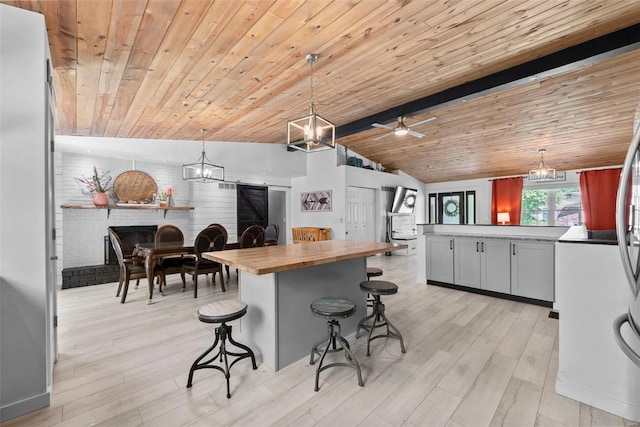 kitchen with wood counters, open floor plan, a brick fireplace, decorative light fixtures, and light wood finished floors
