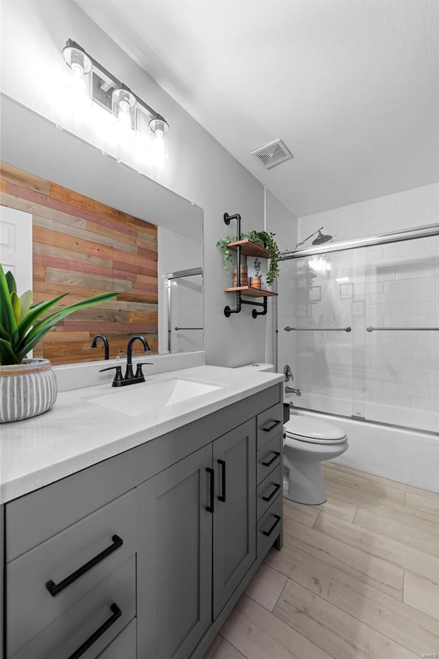 bathroom with wooden walls, vanity, toilet, and bath / shower combo with glass door