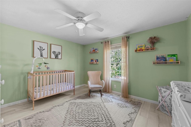 bedroom with a nursery area, wood finished floors, a ceiling fan, a textured ceiling, and baseboards