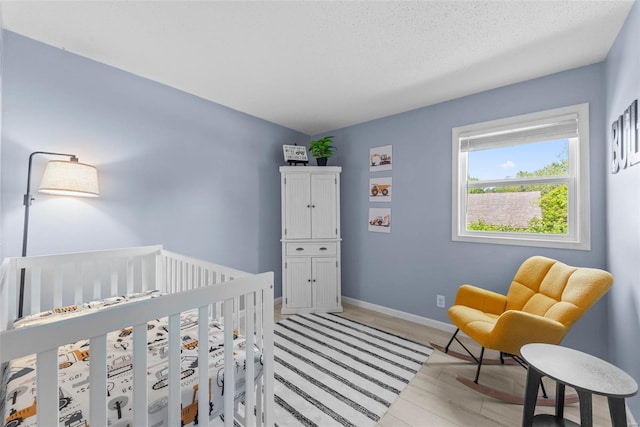 bedroom with light wood-style flooring, baseboards, and a crib