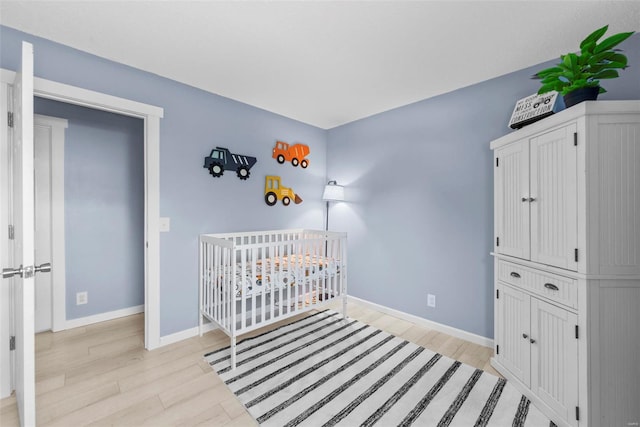 bedroom with light wood finished floors, baseboards, and a nursery area