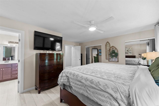 bedroom with two closets, a sink, ensuite bath, baseboards, and a ceiling fan