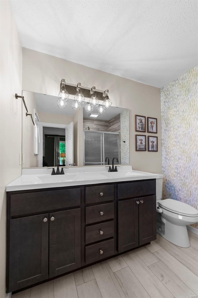 bathroom featuring wallpapered walls, a shower stall, a textured ceiling, double vanity, and wood tiled floors