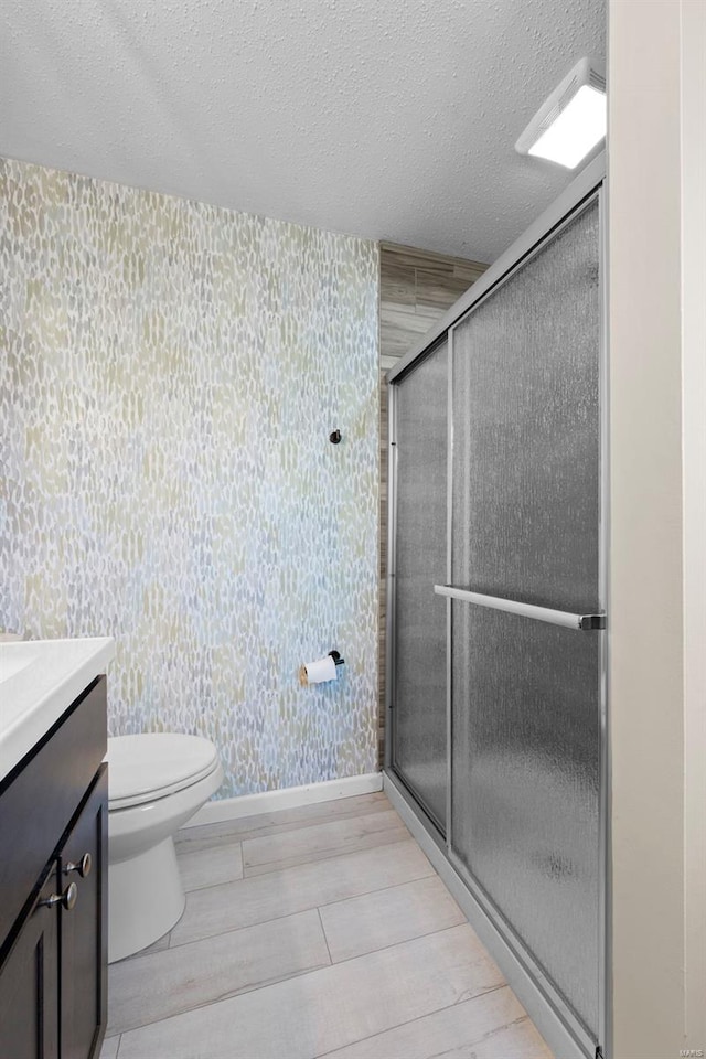 full bath featuring wallpapered walls, a textured ceiling, a stall shower, toilet, and vanity
