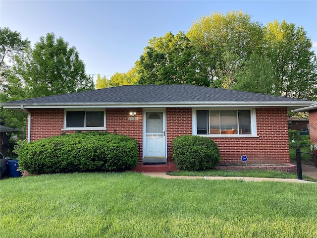 ranch-style home with a shingled roof, brick siding, and a front yard
