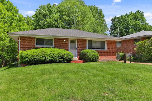 ranch-style home with brick siding, a front yard, and a shingled roof