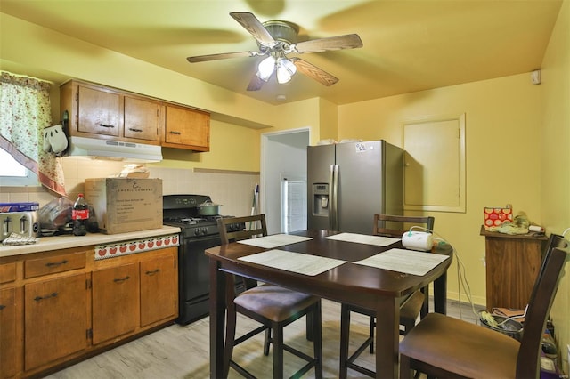 kitchen with black gas range, under cabinet range hood, stainless steel fridge, and brown cabinets