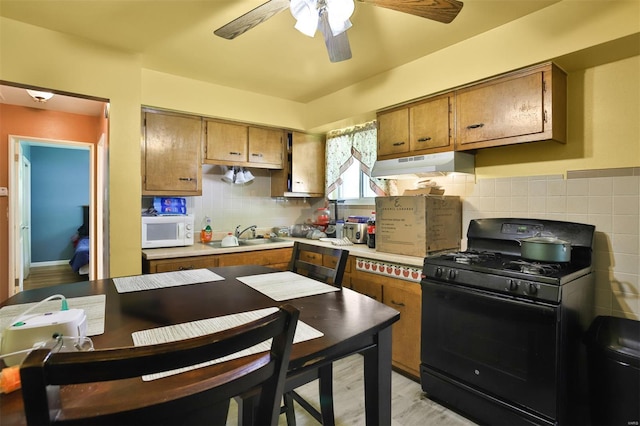 kitchen featuring black gas range oven, under cabinet range hood, white microwave, a sink, and brown cabinetry