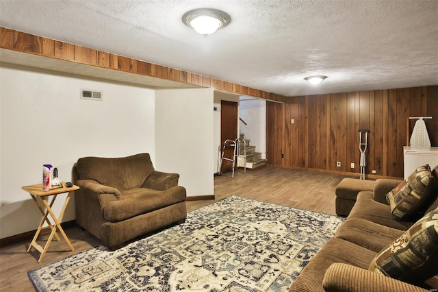 living area with baseboards, stairs, a textured ceiling, wood finished floors, and wood walls
