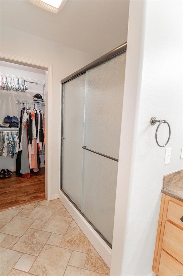 full bath with a stall shower, vanity, a spacious closet, and stone finish floor