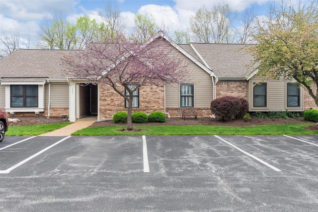 view of front of property with brick siding, a shingled roof, and uncovered parking